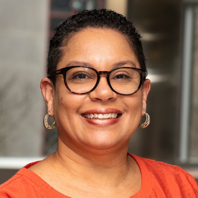 Necie Liggeons smiling in a professional headshot wearing glasses and gold hoop earrings