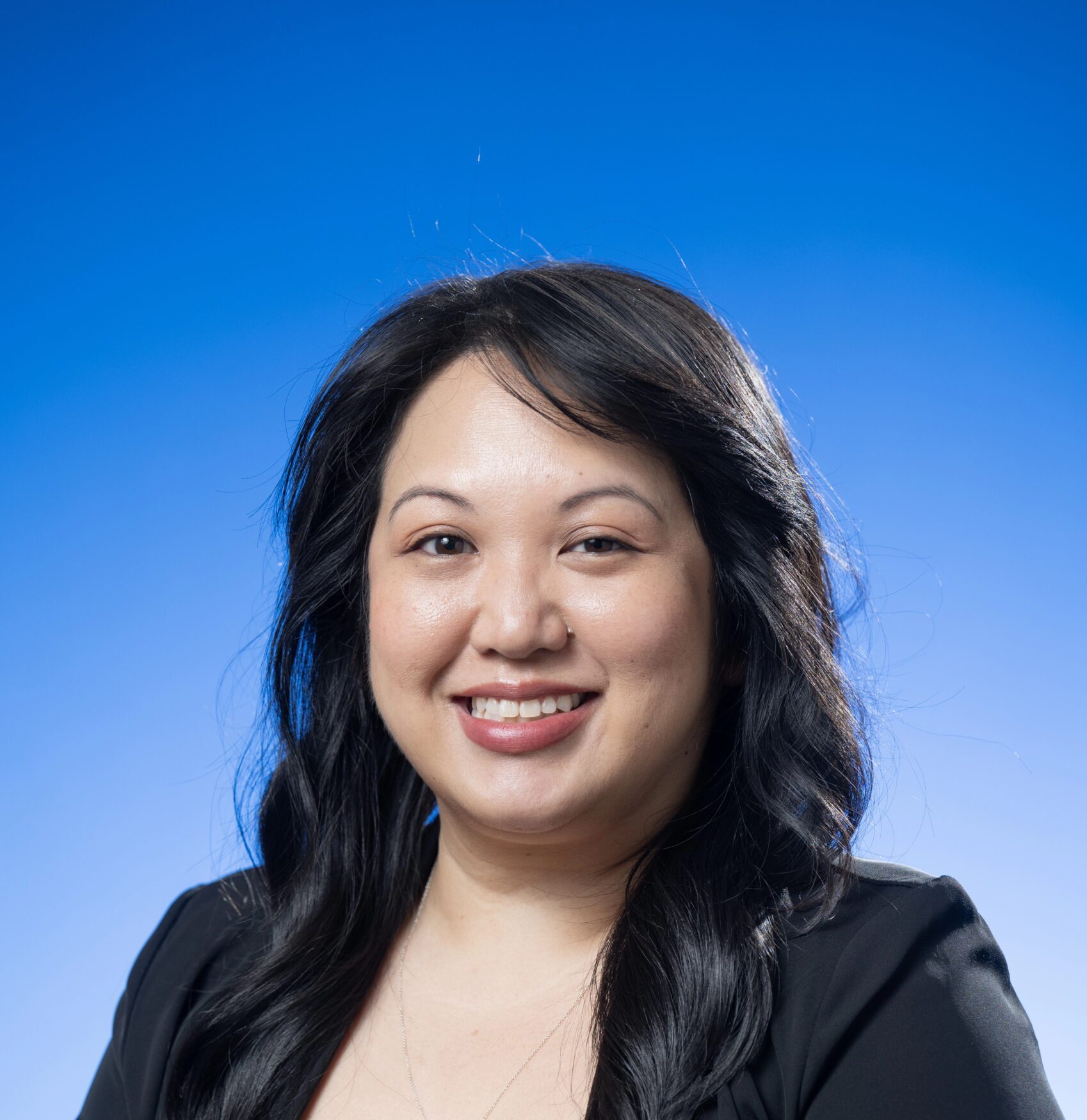 Woman smiling in a black blazer and gray blouse against a blue background