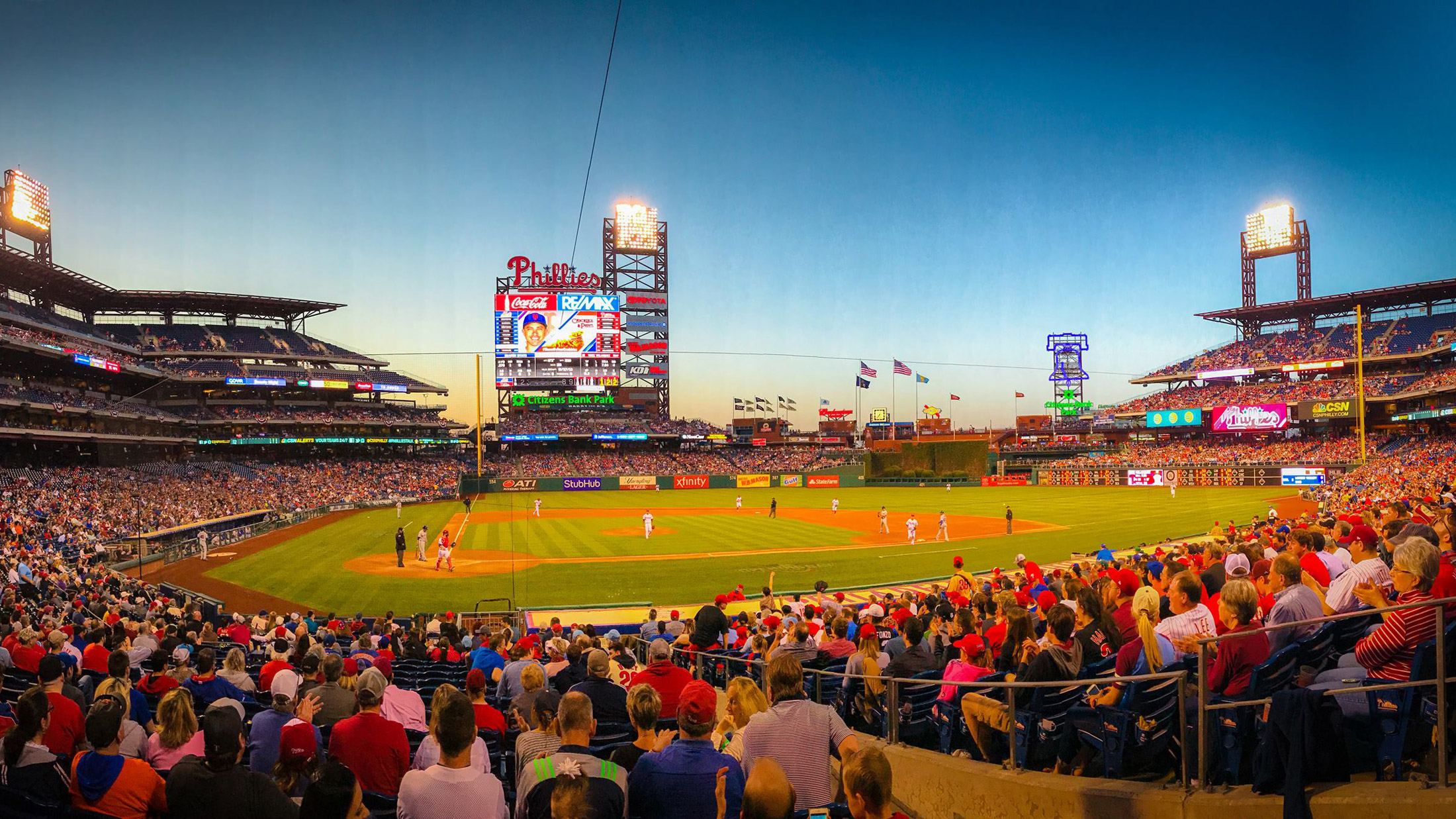 The Phillies stadium from the perspective of someone in the stands during a game at sunset. View of the scoreboard and field.
